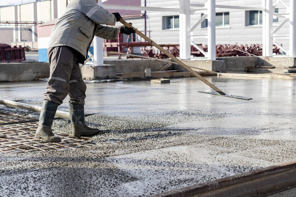 Bouwvakker nivelleren een gegoten betonnen vloer in een industriële werkplaats. Benen in laarzen in beton. Oppervlaktebeton. Monolithisch gewapend betonwerk - Foto, afbeelding