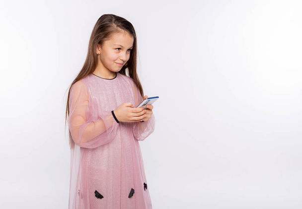 Caucasian kid girl look at screen of mobile phone watching video or typing text, isolated over white background free space for you text - Foto, Imagen