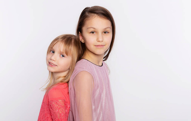 Kaksi tyylikäs ystäviä tai siskoja lapsi tytöt seisovat selkä toisiaan. Tytöt yllään vaaleanpunainen mekko ja seisoo takaisin eristyksissä valkoisella taustalla - Valokuva, kuva