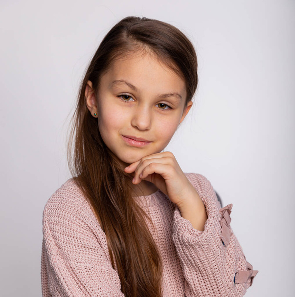 Portret van een vrolijk lachend meisje. Schattig 8 jaar oud meisje gezicht uitdrukking dragen roze trui geïsoleerd over grijze achtergrond - Foto, afbeelding