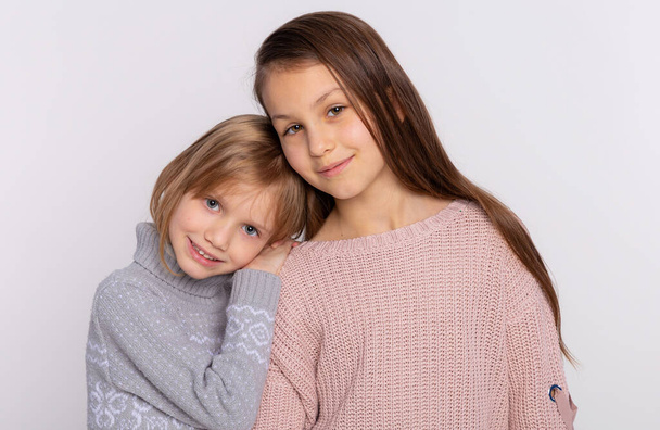 Best friends or sisters happy together stands closely each other resting hand on her friends shoulder. Smiling girls wear knitted sweaters leans at shoulder of friend - Photo, Image
