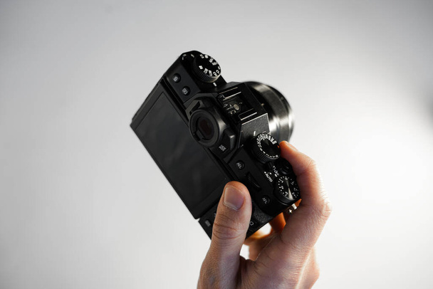 un hombre sostiene una cámara SLR moderna compacta en su mano sobre una vista superior de fondo blanco - Foto, imagen