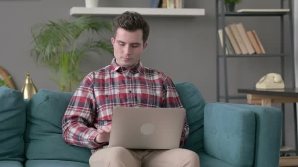 Férfi laptoppal mutatja hüvelykujját a kanapén  - Felvétel, videó