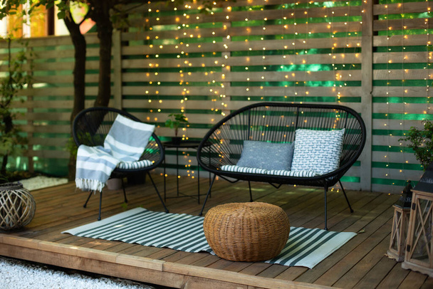 Külső terasz zöld növényekkel, kanapéval és lámpákkal. Hangulatos hely a teraszon vagy erkélyen. Belső fából készült veranda kerti fotellel és asztallal. Nyári társalgó kerti bútorokkal a kertben. - Fotó, kép