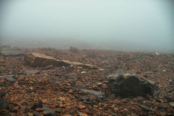 Stone field in dense fog in highlands. Empty stone desert in thick fog. Zero visibility in mountains. Minimalist nature background. Dark atmospheric foggy mountain landscape. Lichens on sharp stones. - Photo, Image