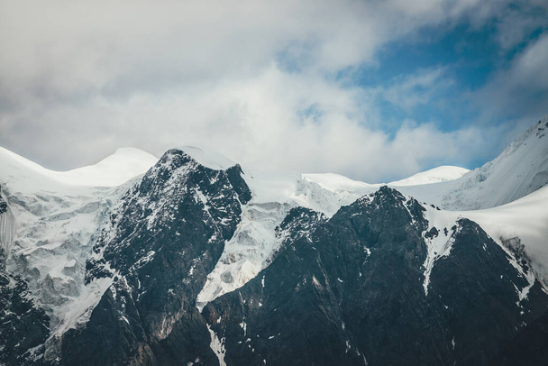 曇り空に素晴らしい雪の山の頂上と素晴らしい山の風景。氷河と高い山と大気中の曇りの風景。雪の大きな山。曇り空の美しい雪の山. - 写真・画像