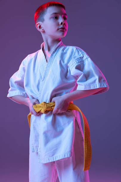 Serious kid, little boy, taekwondo or karate athletes in doboks posing isolated on very peri color background in neon. Concept of sport, martial arts - Valokuva, kuva