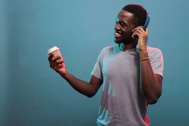 Χαλαρός άνθρωπος απολαμβάνοντας μουσική mp3 στα ακουστικά και το φλιτζάνι του καφέ - Φωτογραφία, εικόνα