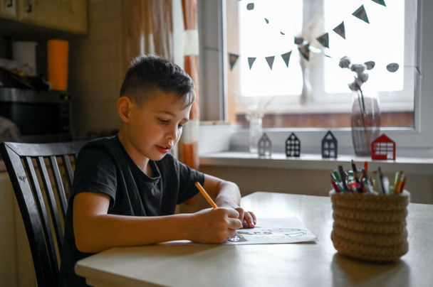 a ten-year-old boy at home at the table draws with colored pencils - Photo, Image