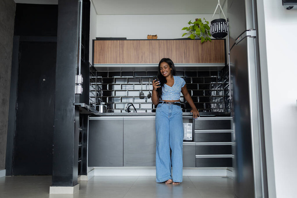 Joven mujer negra trabajando en casa con smartphone en la cocina de su apartamento. Concepto de oficina.  - Foto, Imagen