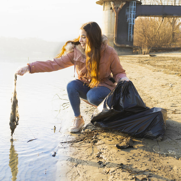 jonge vrouw schoonmaken van het water van plastic afval - Foto, afbeelding
