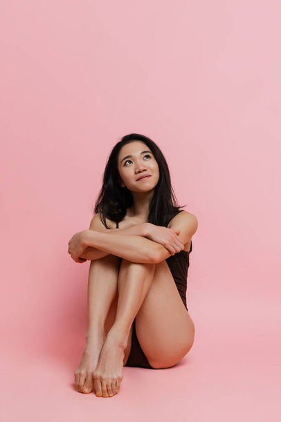 Beautiful young woman tenderly posing in bodysuit isolated over pink studio background - 写真・画像