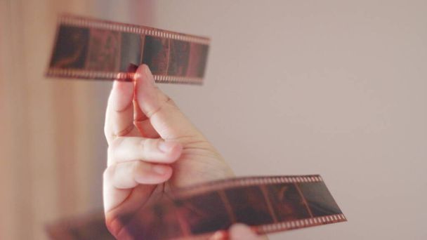 La mano de una mujer sosteniendo una película de 35 mm y brillando en la luz fuera de la habitación. - Foto, Imagen