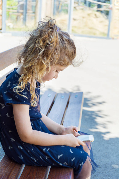 Toddler Girl Sitting Hunched Over on a Bench and looking her mobile phone .Bad Body Posture - Foto, Imagen