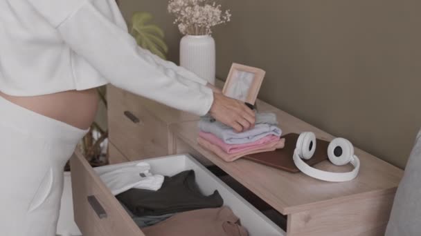 Gehakte slow mo shot van aanstaande moeder zetten kleine baby kleding in lade thuis, streelde haar buik met tederheid - Video