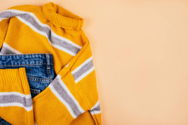 トレンド秋のファッションフラットレイで黄色のセーターとベージュの背景に隔離された青いジーンズ. - 写真・画像