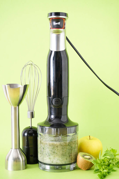 Misturador de mão elétrica de plástico preto e acessórios com frutas e smoothie pronto em fundo verde, verticalmente. - Foto, Imagem