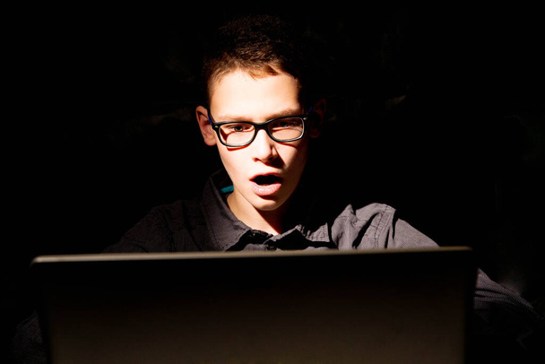 Niño delante de fondo oscuro en el ordenador portátil iluminado selectivamente - Foto, imagen