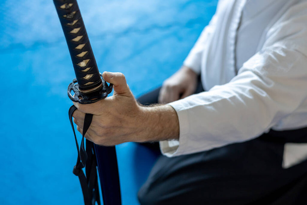 de hand van een man in een kimono houdt een zwaard vast, een vechter van vechtkunst en zijn zwaard. - Foto, afbeelding