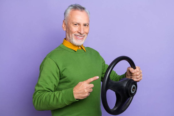 Photo of cheerful man pensioner dressed green pullover pointing steering wheel isolated purple color background - Fotografie, Obrázek