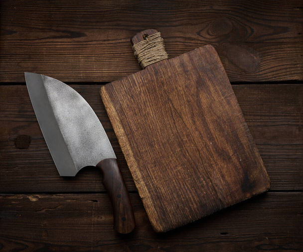 metal kitchen knife and empty wooden cutting board on a table made of brown wooden boards, top view - Photo, Image