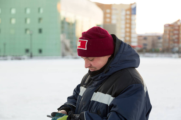 A man in a work overalls looks at the phone - Valokuva, kuva