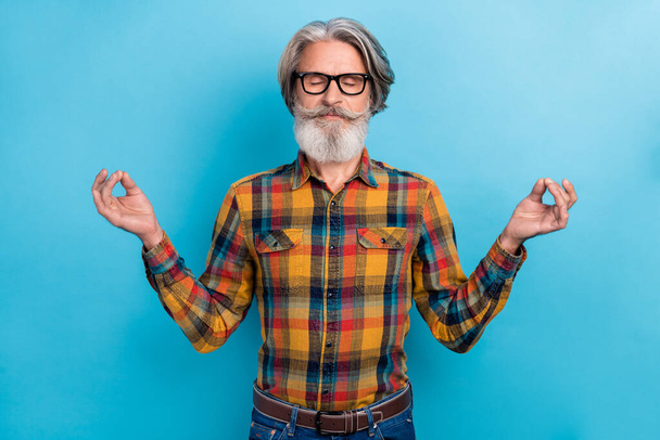 Photo of dreamy man pensioner dressed checkered shirt glasses practicing yoga closed eyes isolated blue color background - 写真・画像