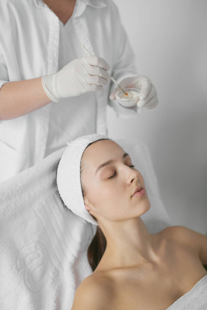 Young beautiful healthy woman's face. Medicine and cosmetology. Doctor's hands in white gloves. Pure nude colors. Nice lips, long neck. Clear skin. Brown hair. Facial mask. Peeling. Skin and body care. Face building. Massage - Photo, image