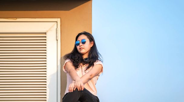 Sun Glasses Asian woman is sitting on the rooftop barricade cement (not dangerous because the opposite site is rooftop floor as well) in front of empty sky. - Fotografie, Obrázek