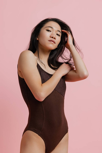Portrait of tender young woman in brown bodysuit posing isolated over pink studio background - Φωτογραφία, εικόνα