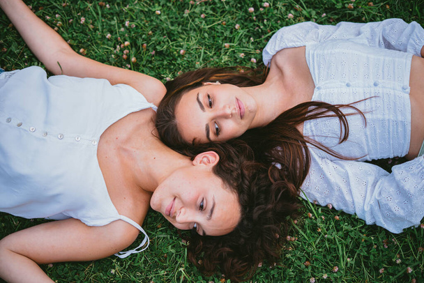 Two relaxed girls laying down on the grass in a park while they are resting - 写真・画像