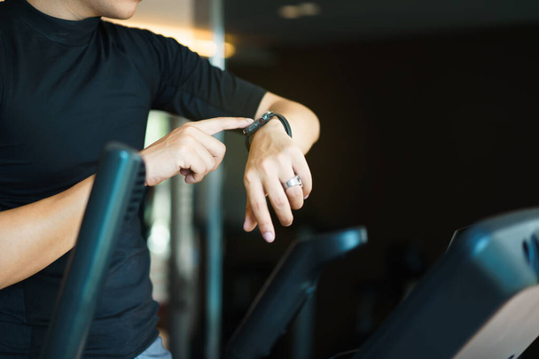 Happy sportsman using a smartwatch or exercise tracker on his wrist to track an exercise, sport man touching a smartwatch screen while exercising on a elliptical exercise machine. Serious workout. - Foto, Imagen