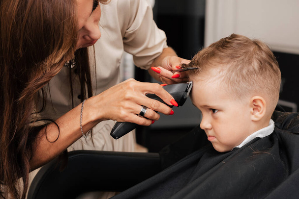 Shooting in a beauty salon. A barber cuts the hair of a little boy with a machine. - Photo, image
