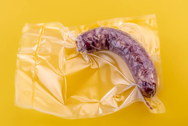 Italian salame sausage in vacuum packed sealed for sous vide cooking isolated on yellow background in top view - Фото, зображення