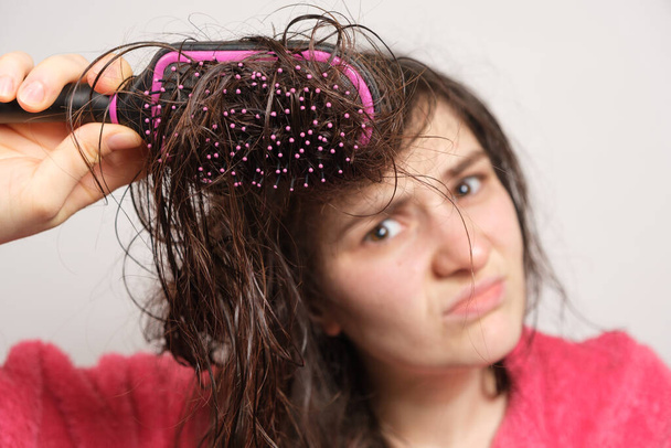 Una mujer trata de peinarse el cabello enredado y húmedo. Cuidado del cabello en casa, caída del cabello y sección. - Foto, imagen