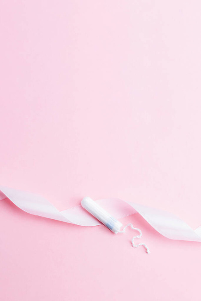 Feminine hygiene menstrual tampon. Pink ribbon with menstrual tampon on pink background. Sanitary hygiene concept. Menstruation feminine period. Gynecological menstruation cycle banner. Copy space - Zdjęcie, obraz