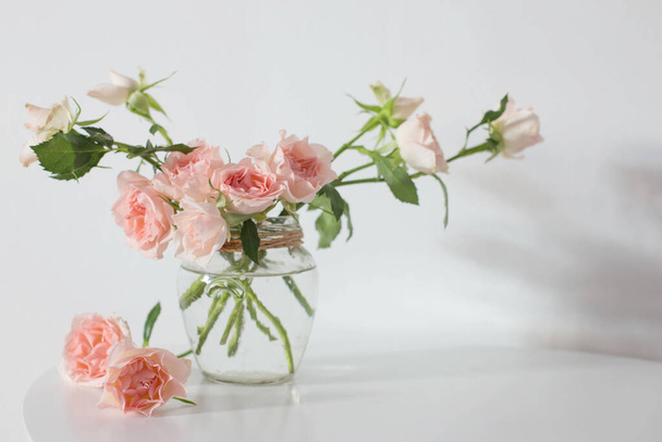 pink roses in glass jar on white modern table on background white wall - Valokuva, kuva