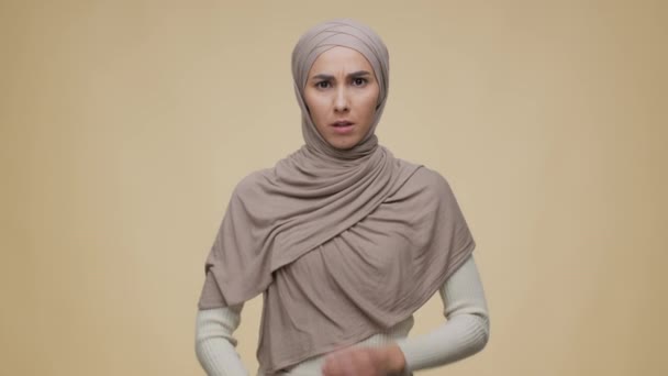 A fiatal, sértett közel-keleti hölgy portréja, aki hagyományos hidzsábot visel, csukott karokkal pózol és mogorván néz ki. - Felvétel, videó