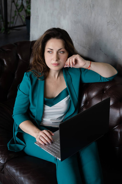 Fernarbeit, Fernausbildung. brünette Frau in grün auf Ledercouch mit Laptop. home office. Arbeit von zu Hause aus - Foto, Bild