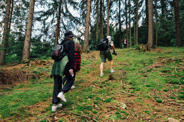 Группа молодых туристов в стильной повседневной одежде поднимается на гору через лес. Друзья в путешествии прогулятся по лесу. - Фото, изображение