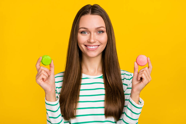 Photo of sweet pretty lady dressed striped shirt choosing green pink cookies isolated yellow color background - Фото, изображение