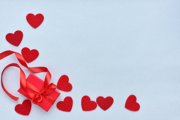 Valentines Day background. Red gift box with ribbon and felt hearts on a pastel blue background. Top view - 写真・画像