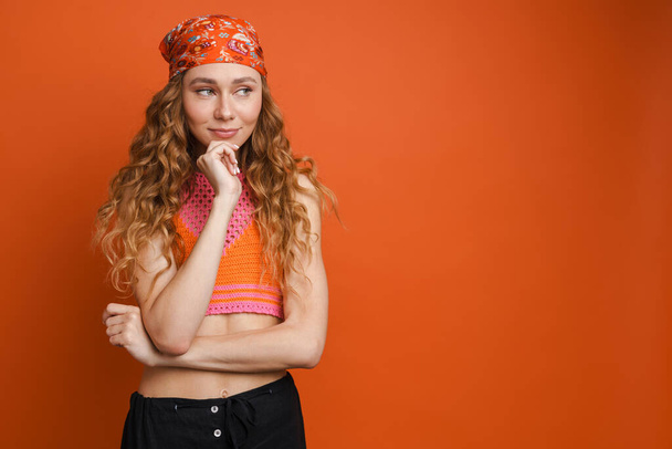 Young ginger woman wearing bandana smiling and looking aside isolated over orange wall - Fotografie, Obrázek