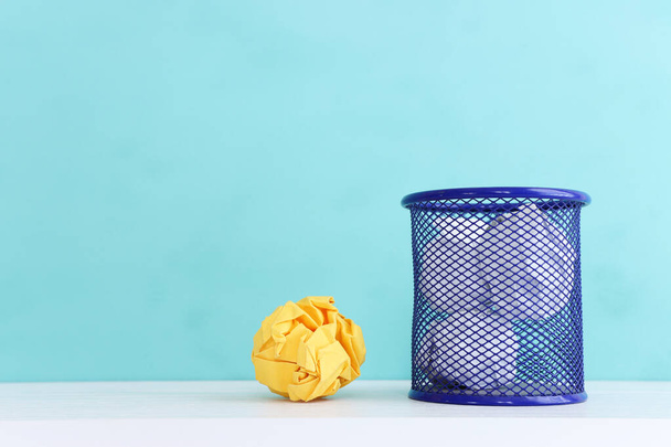 Trash bin with crumpled white and yellow paper over blue background - Foto, Imagen