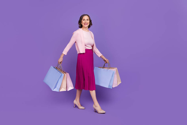 Ganzkörperprofil Porträt der positiven hübschen Dame zu Fuß halten Pakete isoliert auf violettem Hintergrund - Foto, Bild