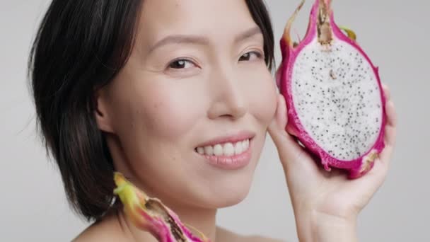 maduro coreano senhora segurando dragão fruta perto do rosto, cinza fundo - Filmagem, Vídeo