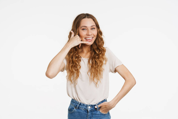 Jonge gember vrouw in t-shirt glimlachen en het maken van handset gebaar geïsoleerd over witte muur - Foto, afbeelding