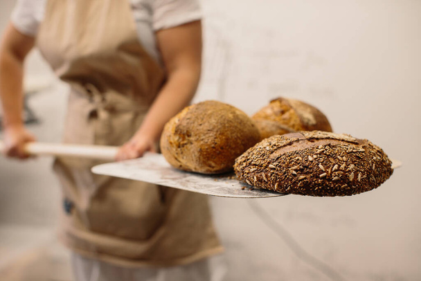 Жінка-пекарня з використанням шкірки, щоб вийняти хліб з печі в пекарні
 - Фото, зображення