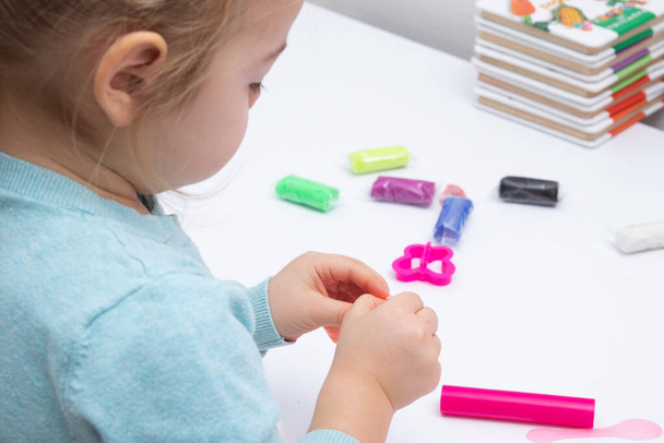 The girl at the table is playing with modeling dough. Children's games for fine motor skills - 写真・画像