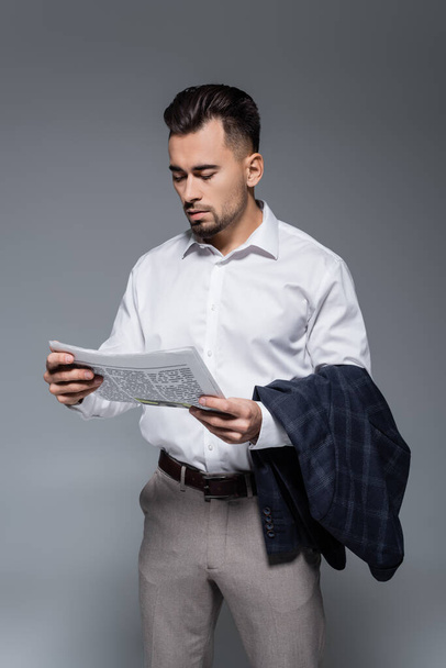 giovane uomo d'affari barbuto in giacca e cravatta leggendo giornale isolato su grigio - Foto, immagini